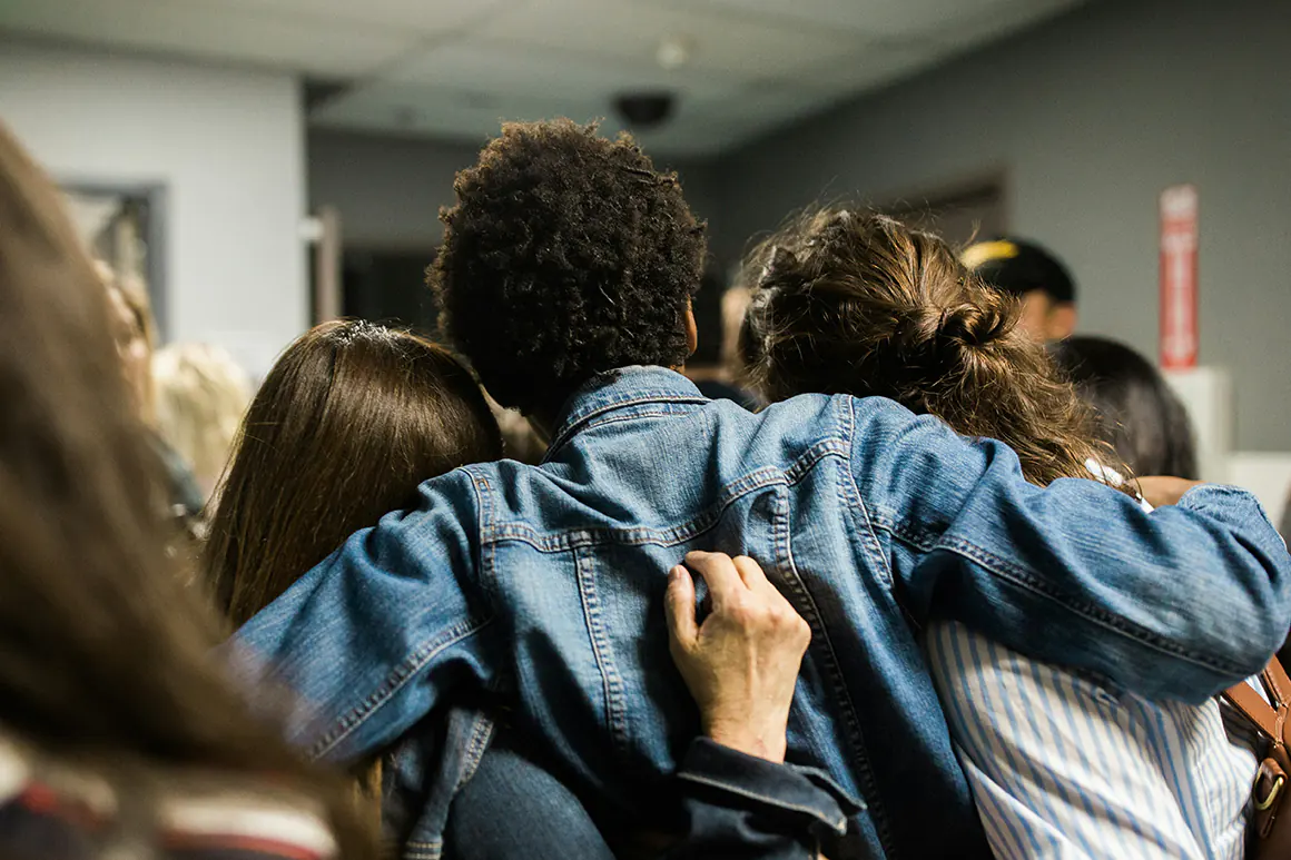 three students in a classroom hugging from behind