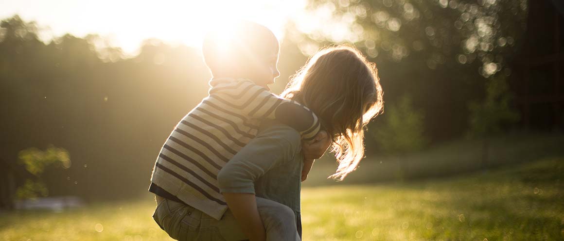 sister and brother piggy back in field