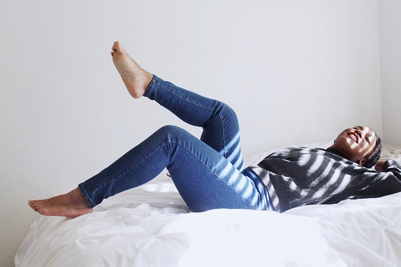 Frau liegt auf dem Bett und streckt Beine in die Höhe