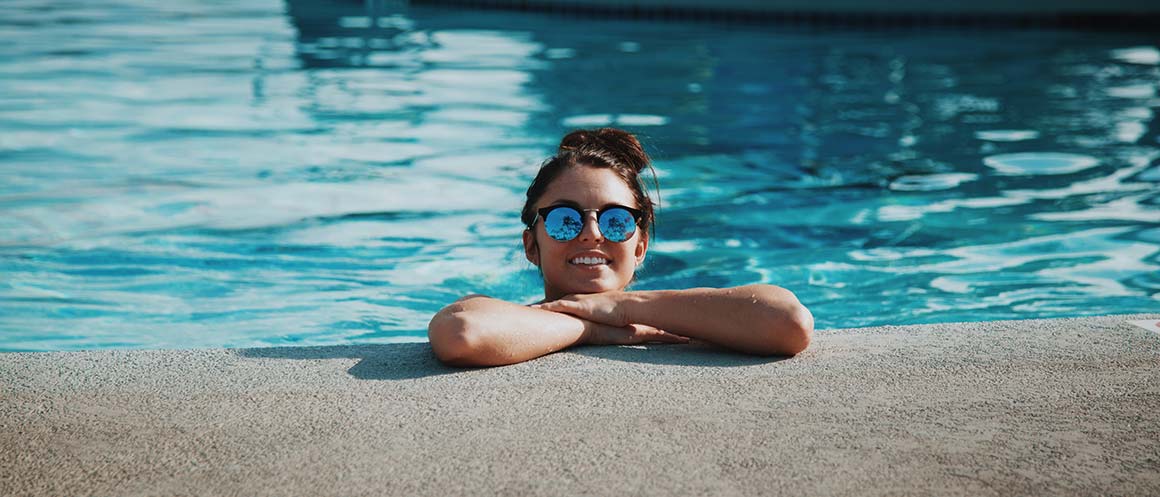 Mujer sonriendo en una piscina bajo el sol con gafas de sol