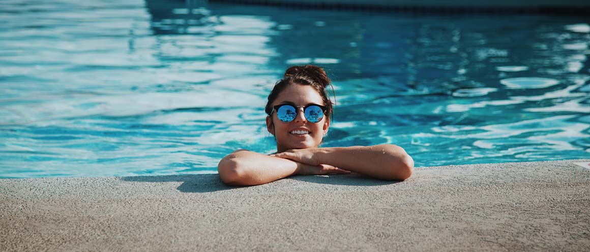 femme souriante dans une piscine au soleil avec des lunettes de soleil