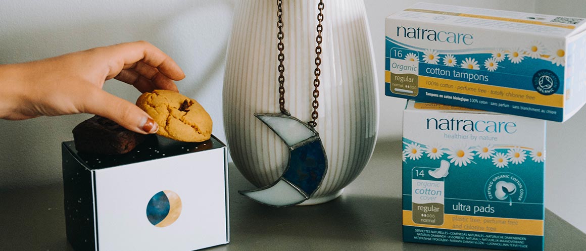 Hand holding a cookie next to a stack of period products