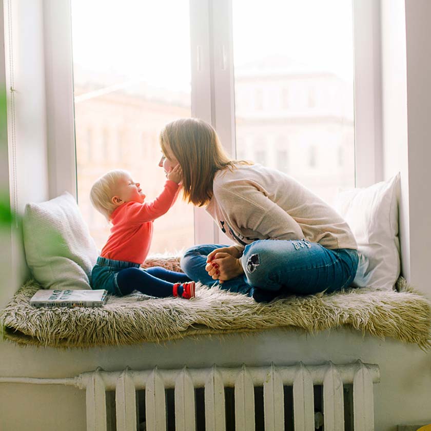 baby with hands on mum's face on windowsill