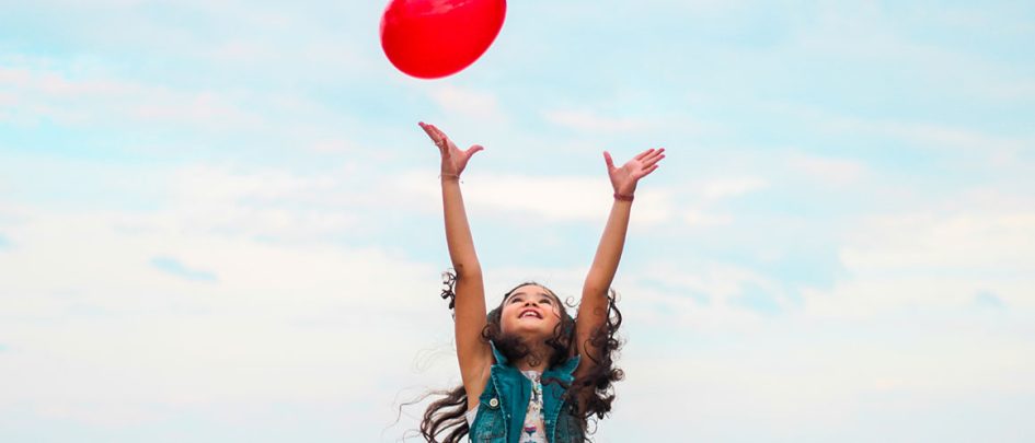 Young girl throwing red balloon in the air