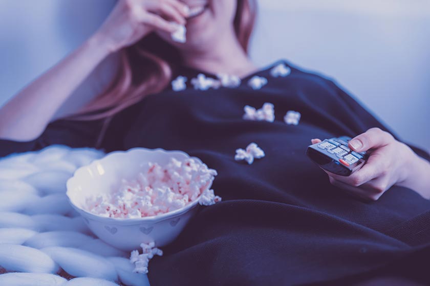 Frau auf Sofa mit Popcorn und Fernbedienung