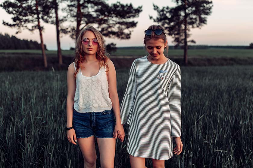 Zwei Mädchen in Sommerkleidung gehen händchenhaltend durch ein Feld