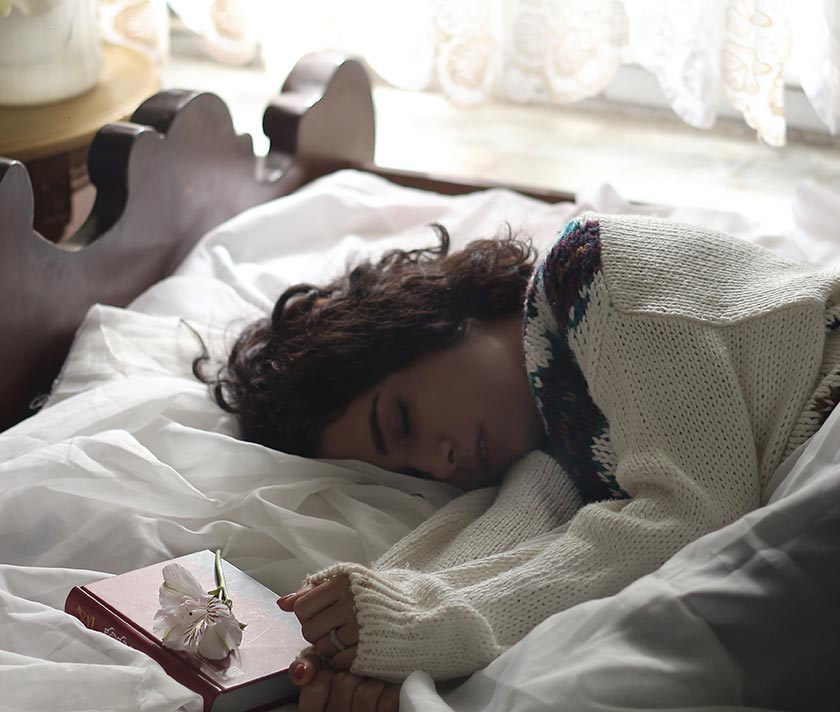 woman in bed sleeping with book and flower