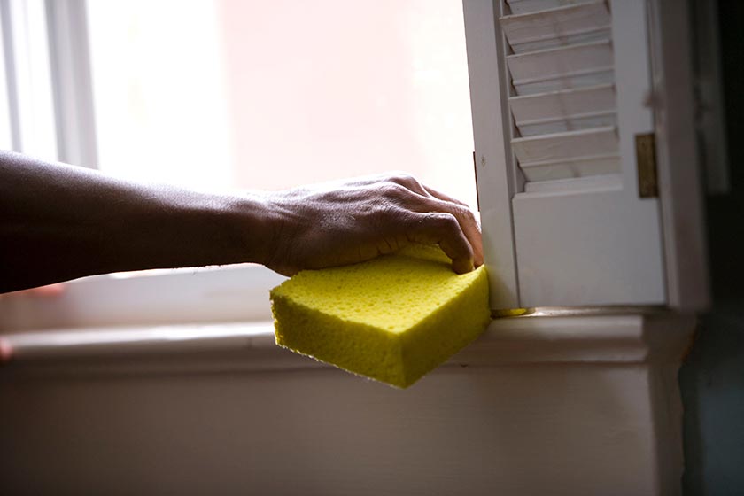person using a sponge to clean windowsill