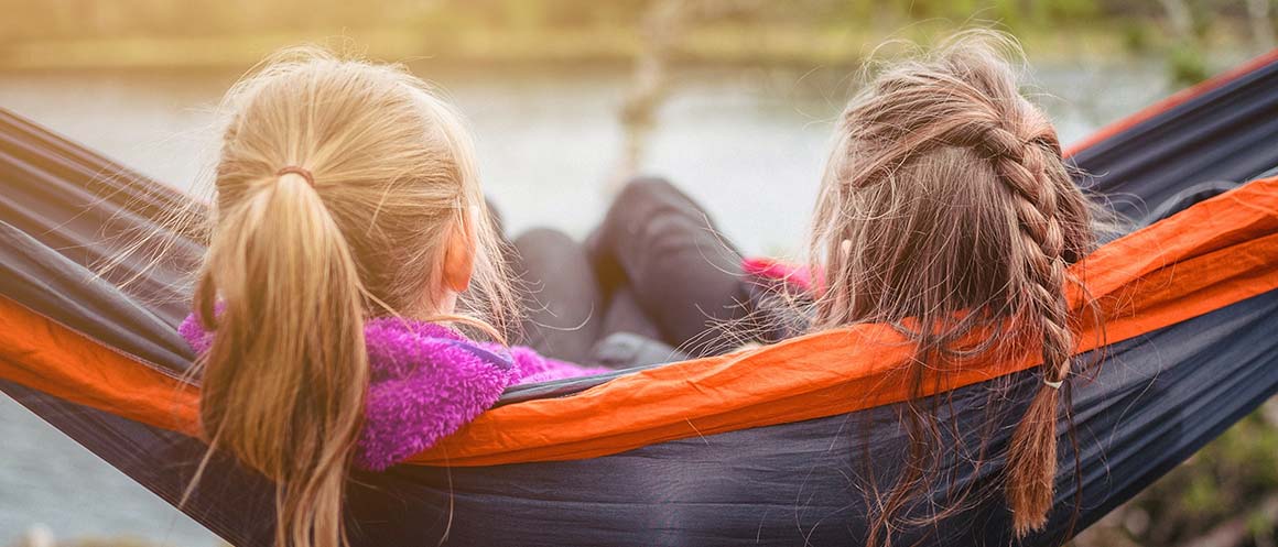 two girls sat in a hammock near water