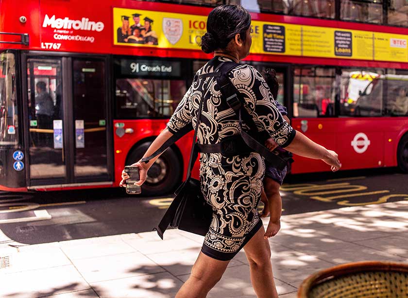 woman with baby in sling walking along a busy street