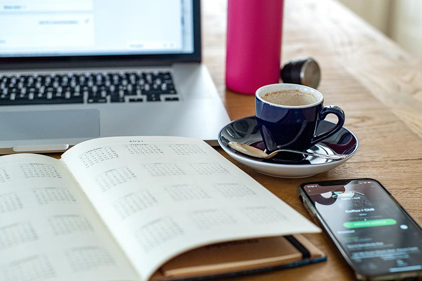 Diary open on table with cup of coffee and laptop