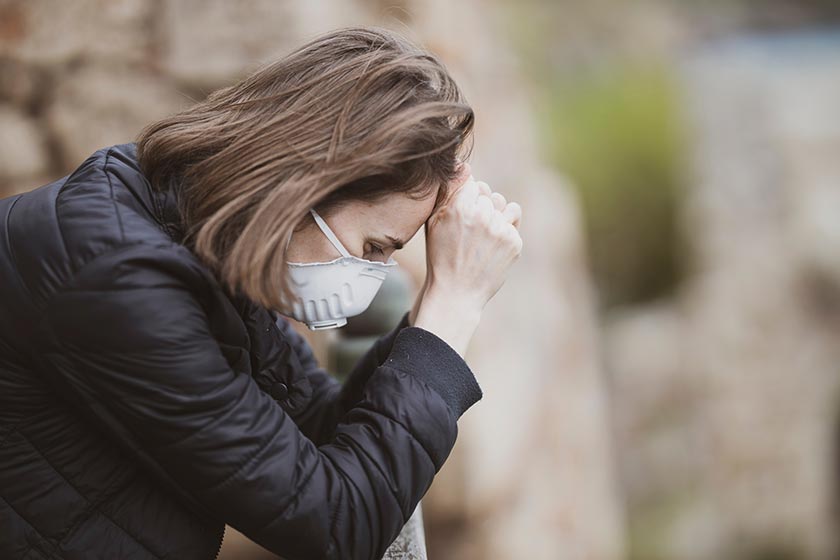 Frau mit Mund-Nasen-Schutz stützt Kopf verzweifelt in die Hände