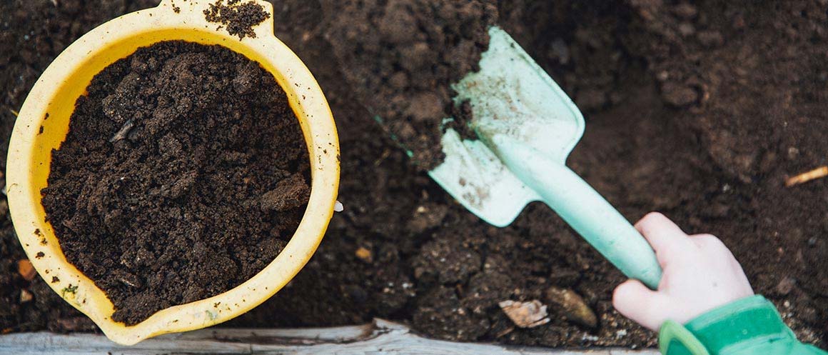 a hand and trowel digging through compost