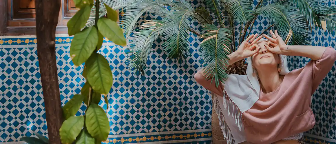 person surrounded by plants looking up and making glasses with their hands on their face