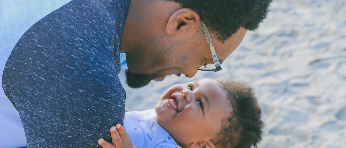 Een vader die een baby vasthoudt op een strand